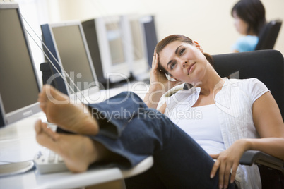 Woman in computer room with feet up thinking