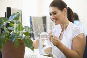 Woman in computer room watering plant smiling