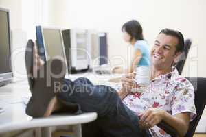 Man in computer room with feet up drinking coffee and smiling