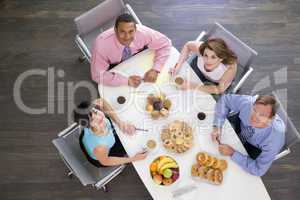 Four businesspeople at boardroom table with breakfast smiling