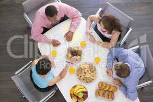 Four businesspeople at boardroom table with breakfast