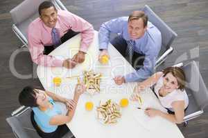 Four businesspeople at boardroom table with sandwiches smiling