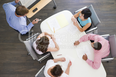 Four businesspeople at boardroom table watching presentation