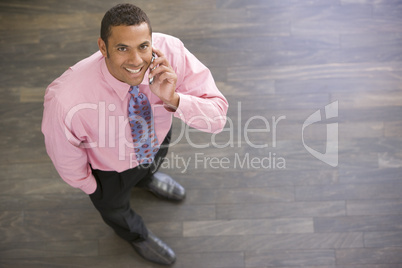 Businessman standing indoors using cellular phone smiling