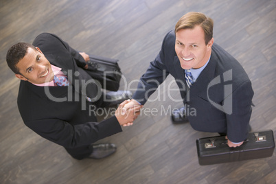 Two businessmen indoors shaking hands smiling
