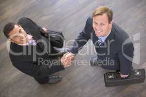 Two businessmen indoors shaking hands smiling