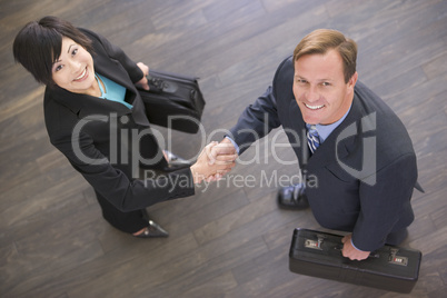 Two businesspeople indoors shaking hands smiling