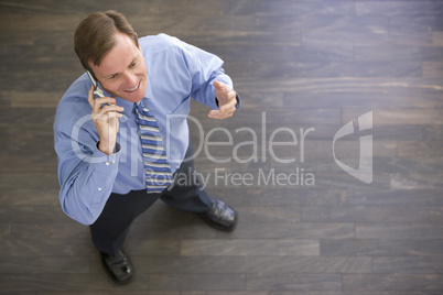 Businessman standing indoors using cellular phone and smiling