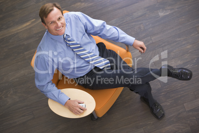 Businessman sitting indoors with cellular phone smiling