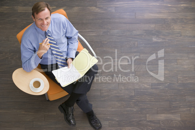 Businessman sitting indoors with coffee and folder smiling