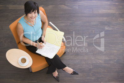 Businesswoman sitting indoors with coffee and folder smiling