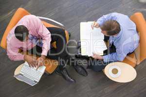 Two businessmen sitting indoors with coffee laptop and folder