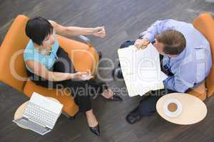 Two businesspeople sitting indoors with coffee laptop and folder