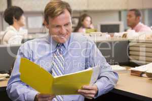 Businessman in cubicle with folder smiling