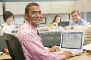Businessman in cubicle using laptop and smiling