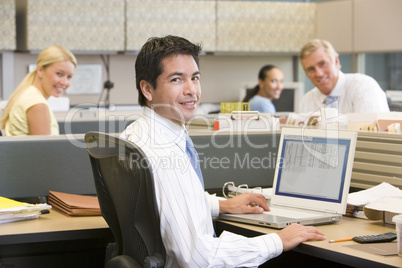 Businessman in cubicle with laptop smiling