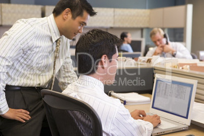 Two businessmen in cubicle looking at laptop
