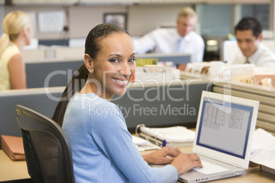 Businesswoman in cubicle using laptop smiling