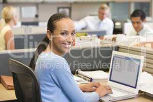 Businesswoman in cubicle using laptop smiling