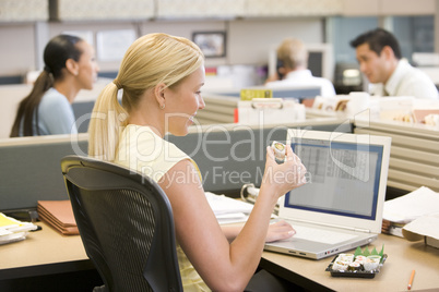 Businesswoman in cubicle using laptop eating sushi