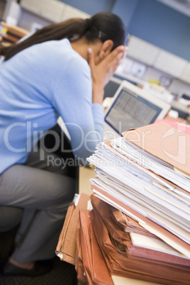 Businesswoman in cubicle with laptop and stacks of files