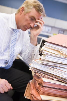 Businessman in cubicle with laptop and stacks of files