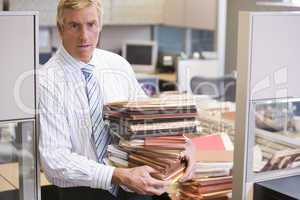 Businessman standing in cubicle holding stacks of files