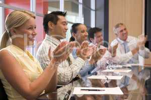 Five businesspeople at boardroom table applauding and smiling
