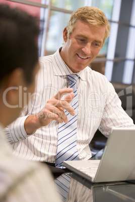 Two businessmen in boardroom with laptop talking