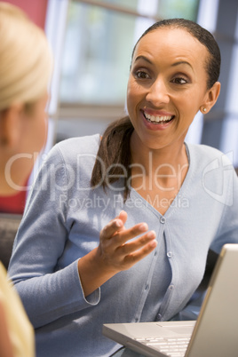 Two businesswomen in boardroom with laptop talking