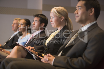Five businesspeople sitting in presentation room with clipboards