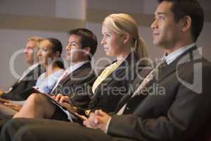 Five businesspeople sitting in presentation room with clipboards