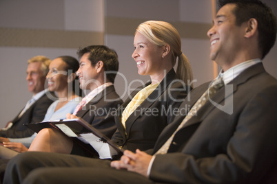 Five businesspeople smiling in presentation room with clipboards