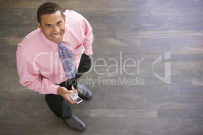 Businessman standing indoors with cellular phone smiling