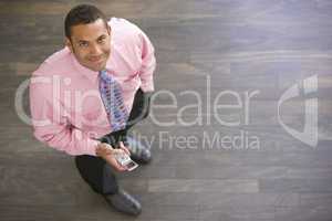 Businessman standing indoors with cellular phone smiling