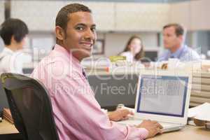 Businessman in cubicle with laptop smiling