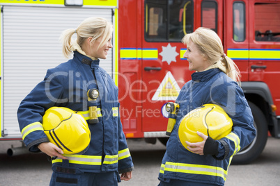 Zwei Feuerwehrfrauen stehen vor einem Löschfahrzeug und schauen sich an