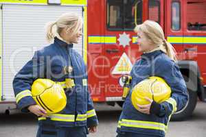 Zwei Feuerwehrfrauen stehen vor einem Löschfahrzeug und schauen sich an