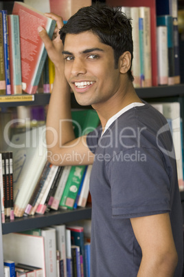 Male college student reaching for a library book