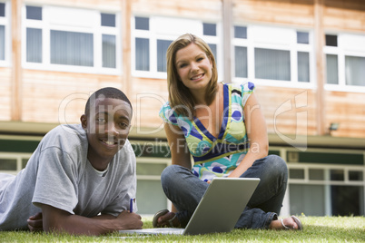 Two college students using laptop on campus lawn