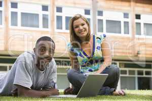 Two college students using laptop on campus lawn