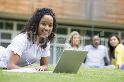 Young woman using laptop on campus lawn, with other students rel
