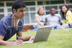 Young man using laptop on campus lawn, with other students relax