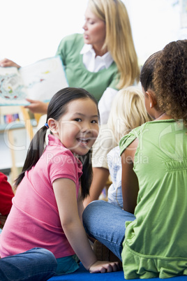 Kindergarten teacher reading to children in library, girl lookin