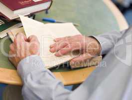 Close-up of mature student's hands turning book page in library