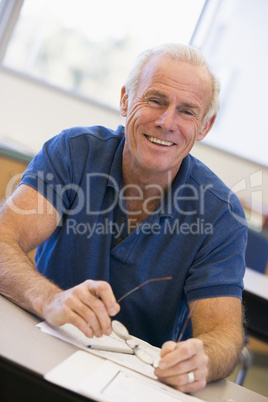 Mature male student holding glasses in class