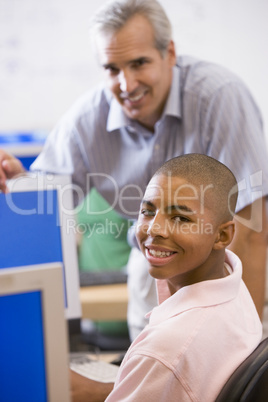 A teacher talks to a schoolboy using a computer in a high school