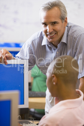 A teacher talks to a schoolboy using a computer in a high school