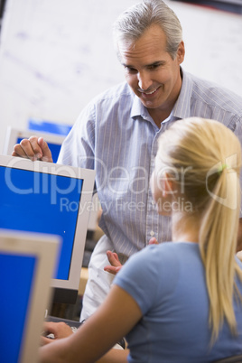 A teacher talks to a schoolgirl using a computer in a high schoo