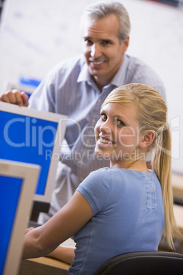 A teacher talks to a schoolgirl using a computer in a high schoo